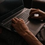 Vagas para Auxiliar Administrativo Remoto Focused close-up of hands typing on a laptop keyboard, showcasing digital work and technology.