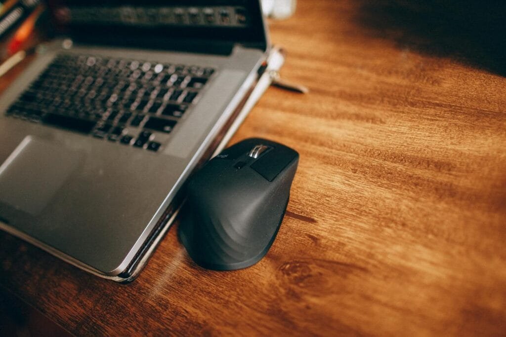 Vagas 100% Remotas na Vobi A wireless mouse and laptop placed on a polished wooden desk, perfect for office and remote work setup.
