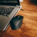 Vagas 100% Remotas na Vobi A wireless mouse and laptop placed on a polished wooden desk, perfect for office and remote work setup.