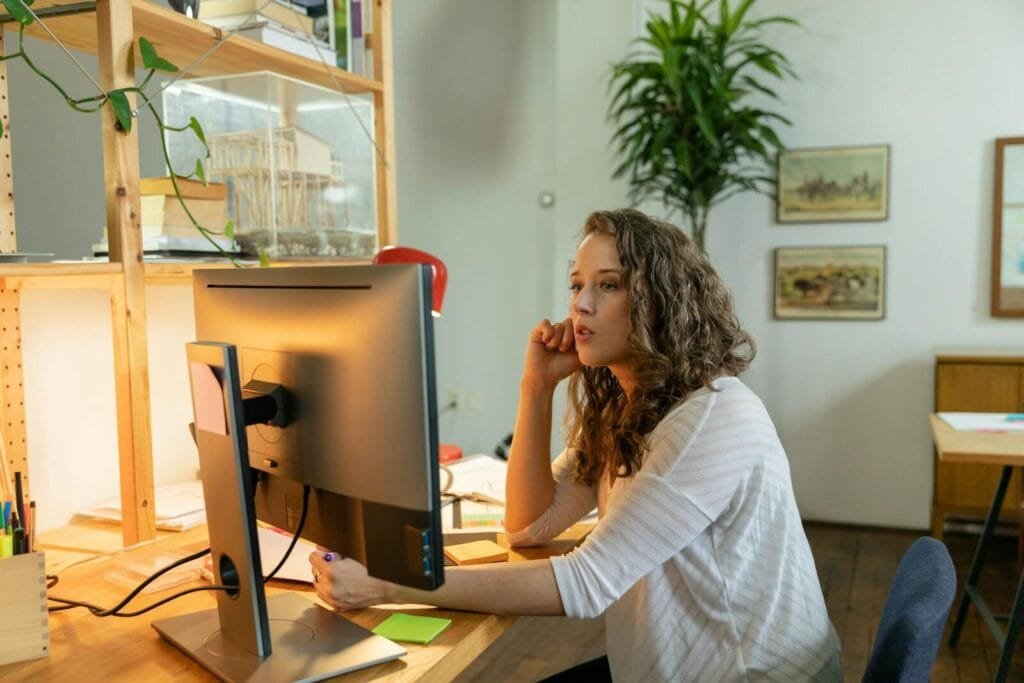 Vagas Remotas na Pantheon  A young woman focuses on her computer in a cozy home office setting, embodying remote work culture.