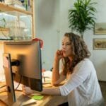Vagas Remotas na Pantheon A young woman focuses on her computer in a cozy home office setting, embodying remote work culture.