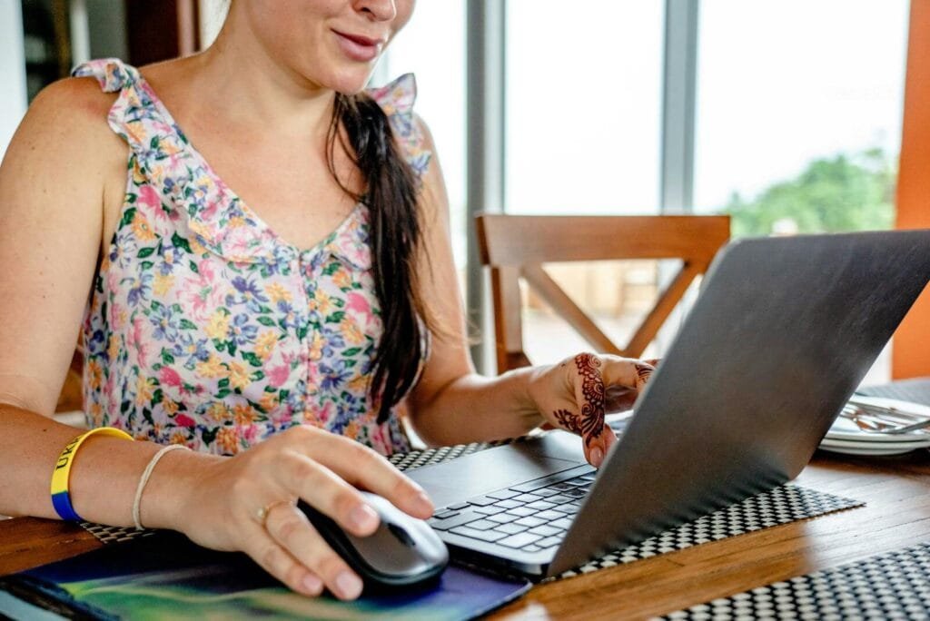 Neogrid contratando para Home Office A woman using a laptop for remote work indoors, featuring a floral dress and henna design.