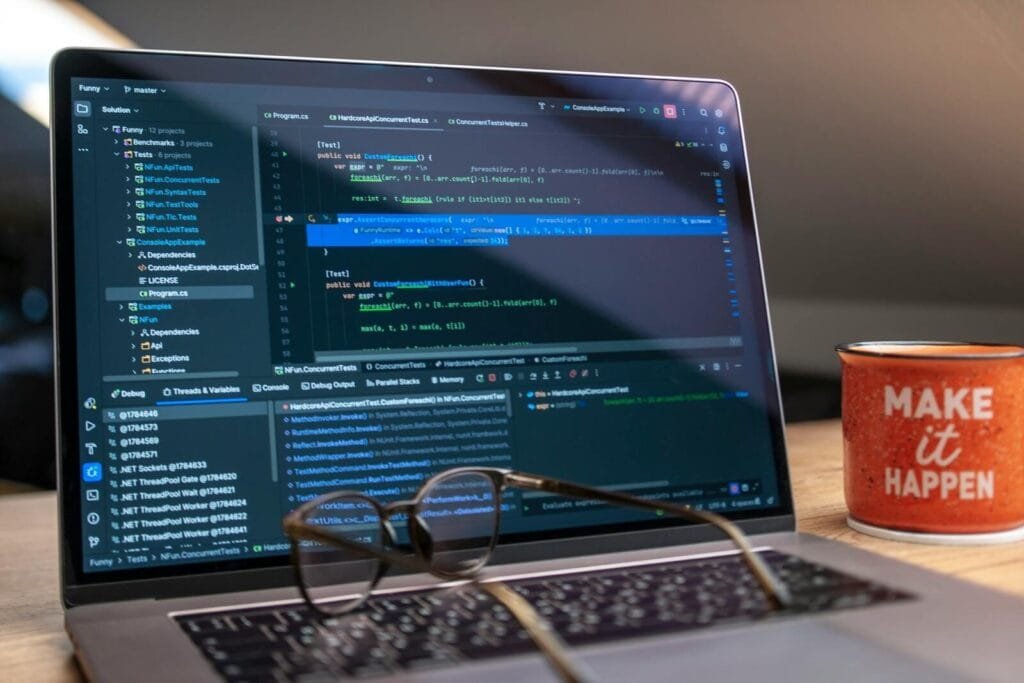 Vagas Remotas na Nexdom, com VA/VR de R$ 950,00 A laptop displaying code editor with a motivational mug that reads 'Make It Happen' on a workspace.
