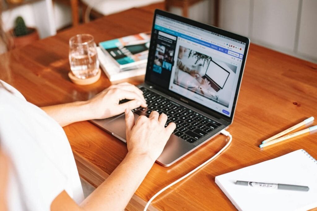 Emprego Remoto na Flash A person working remotely on a laptop at a wooden desk with stationery and a notepad.