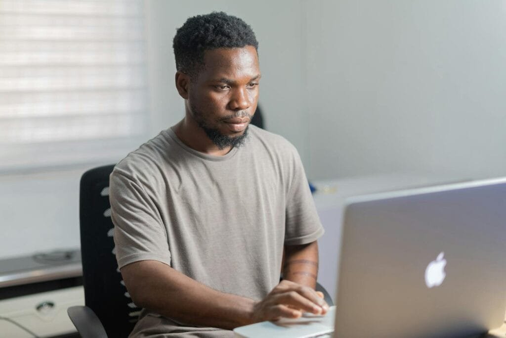 Vagas remotas para Assistente Administrativo e + African American man working remotely on a laptop in a well-lit indoor setting.