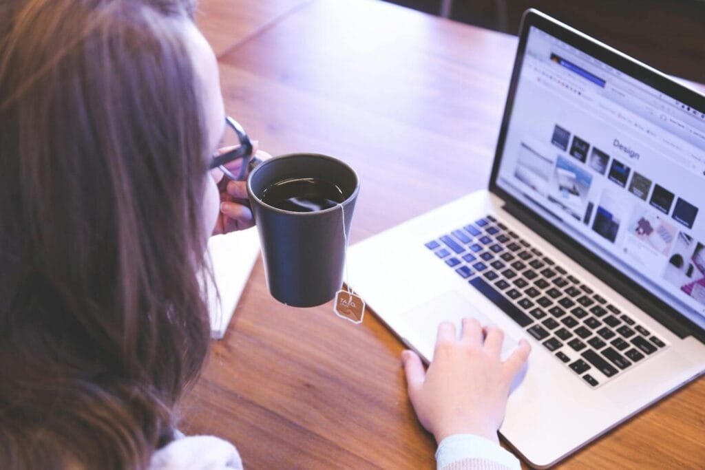 Vinta contrata Home Office com R$ 1.600 de VA/VR e salário até 18.300! A woman enjoys coffee while browsing the web on a laptop at a home office desk.