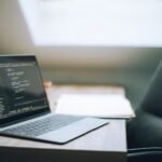 SPC Brasil contratando, VA/VR de R$ 1.300,00 Open laptop displaying code on desk in bright, modern office setting. Ideal for tech and remote work context.