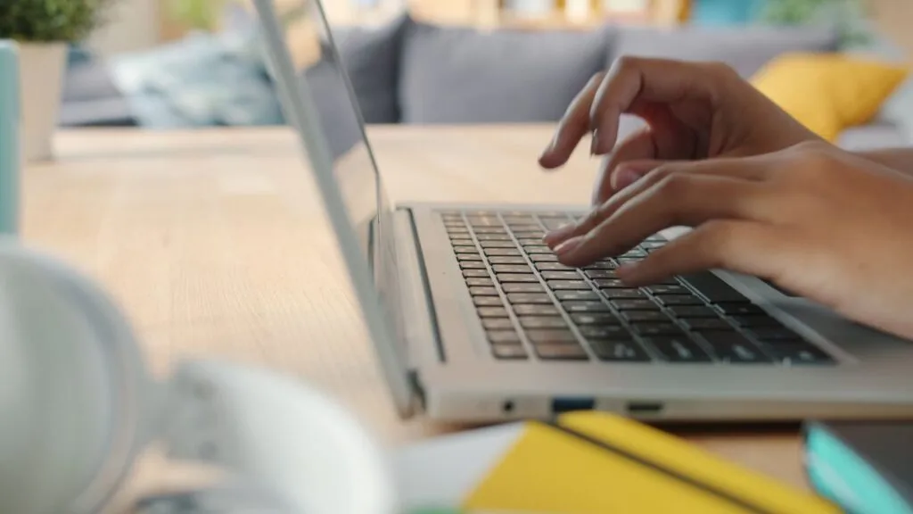  Desenvolvedor Cobol e mais Vagas 100% Remotas! Hands typing on a laptop keyboard indoors with blurred background and natural lighting.