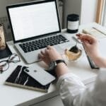Home Office com VA/VR de R$ 1.200,00 A cozy home office scene with a laptop, tea, and workspace essentials.