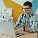 Bhever contrata Home Office, remuneração até R$ 7.000,00 Man wearing glasses typing on a laptop at a desk.