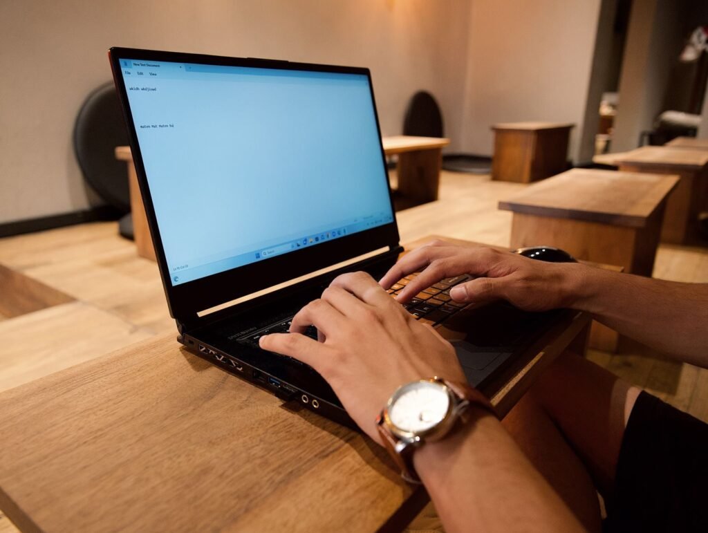 Teletrabalho com VA/VR até R$ 880,00 A person working on a laptop in a modern office setting, focused on typing.