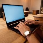 Teletrabalho com VA/VR até R$ 880,00 A person working on a laptop in a modern office setting, focused on typing.