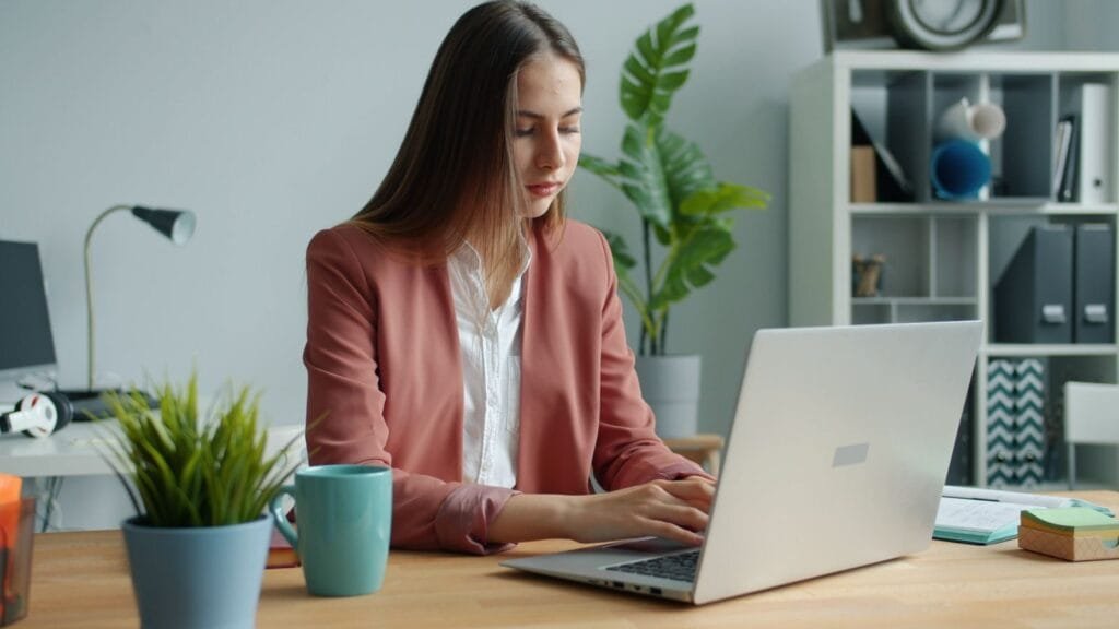 Desenvolvedor Node Júnior e mais Vagas 100% Remotas Confident young woman in business attire working on computer in modern office setting.