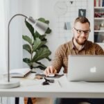 Remotas na ContaJá, R$700,00 de VA/VR e + Adult male working remotely in a stylish home office with a laptop, displaying a modern workspace.