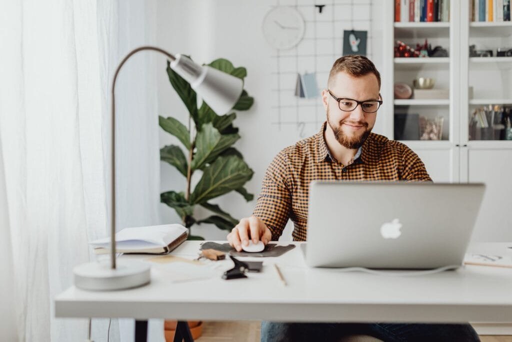 Vagas 100% Remotas na Eureca Adult male working remotely in a stylish home office with a laptop, displaying a modern workspace.