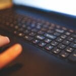 Vagas Remotas na Vetta, com VA/VR de R$ 720 Blurred close-up of hands typing on a laptop keyboard, capturing a focused work moment.