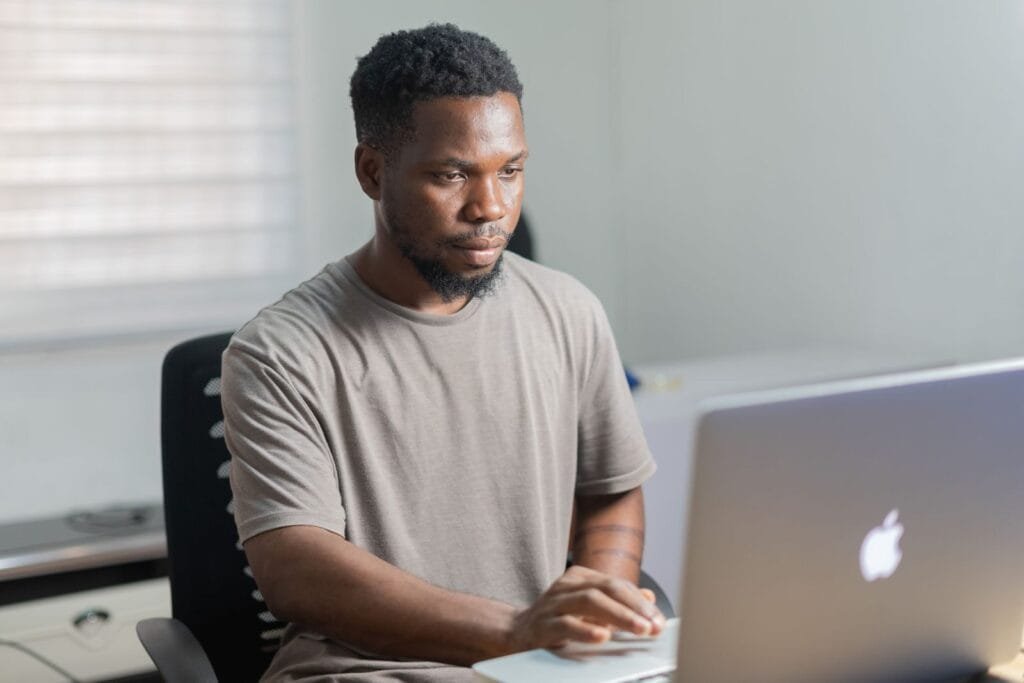 Home Office com R$ 1.000,00 de VA/VR African American man working remotely on a laptop in a well-lit indoor setting.