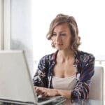 Trabalho Remoto na Spread, VA/VR de R$ 800,00 A woman typing on a laptop in a bright, modern home office setting.