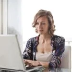Trabalho Remoto na Spread, VA/VR de R$ 800,00 A woman typing on a laptop in a bright, modern home office setting.