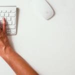 Estágio Financeiro e mais vagas 100% Home Office Close-up of hands typing on a keyboard with a yellow watch on the desk