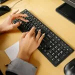 Customer Success com VA/VR de R$ 1.000 Hands typing on a keyboard in an office environment, viewed from above.