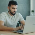 Estágio com VR/VA até R$ 1.500! Man typing on a laptop at a desk.