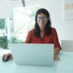 Remotas na OLX com R$ 950 de VA/VR Woman smiles while working on a laptop.
