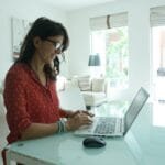 Teletrabalho com VR/VA até R$ 1.500 Woman is working on a laptop at a table.