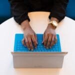 Analista de BI Júnior e + vagas 100% remotas Hands of a person typing on a laptop with a blue keyboard, taken from above, ideal for technology themes.