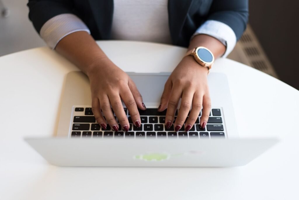 Vagas Remotas com R$ 2.400,00 para posto de trabalho e + benefícios! Woman's hands typing on a wireless laptop at a modern office desk, highlighting technology in business.