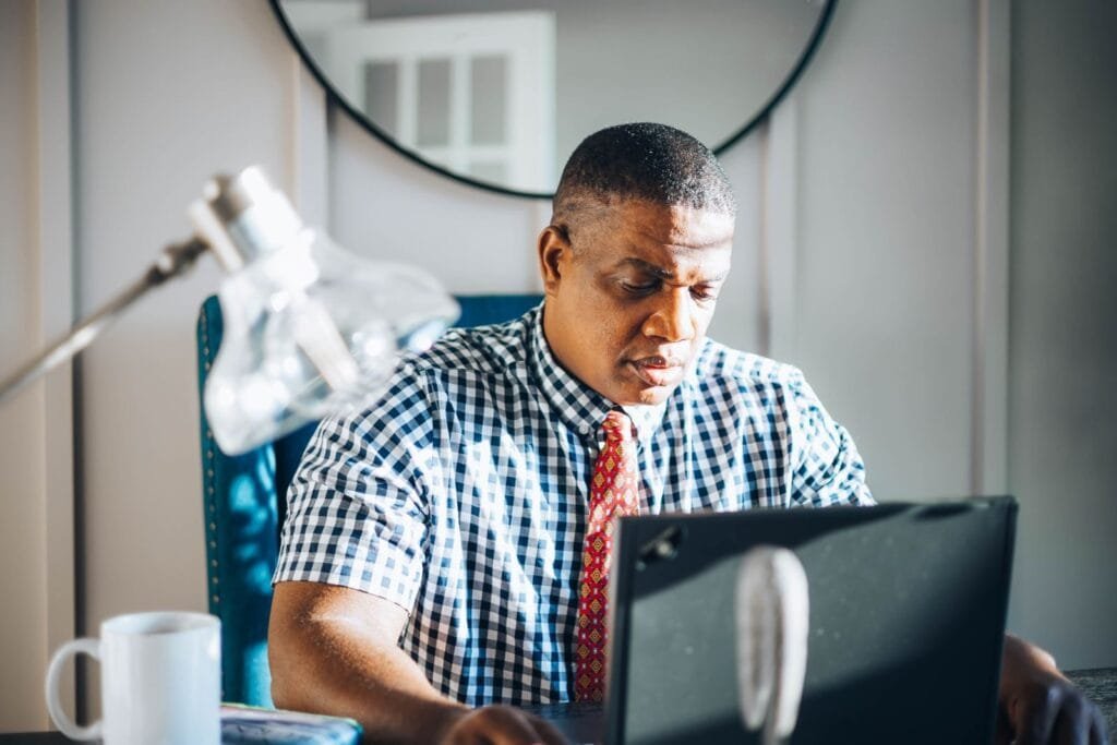 Analista de CX e +Remotas com R$ 780 de VA/VR A concentrated adult man working on his laptop in a bright modern office setting.