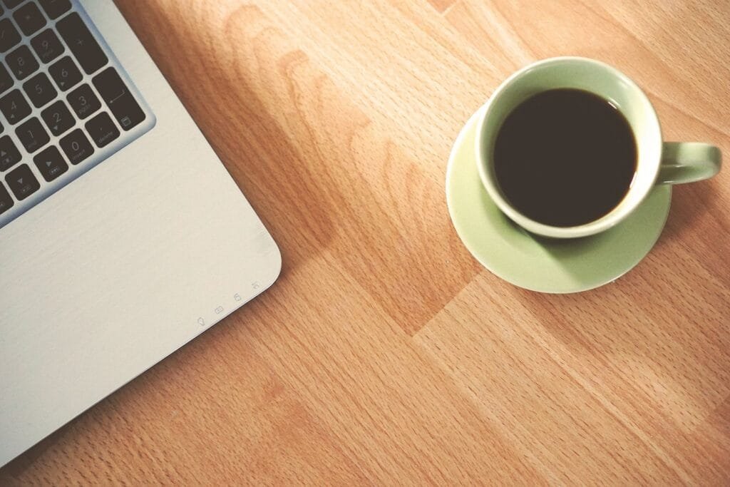 Vagas efetivas (CLT) de emprego 100% remotas A coffee cup and laptop on a wooden desk, creating a cozy workspace vibe.