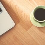 Vagas efetivas (CLT) de emprego 100% remotas A coffee cup and laptop on a wooden desk, creating a cozy workspace vibe.