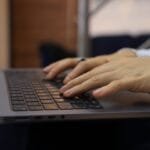Remotas na ContaJá, R$700,00 de VA/VR e + Hands typing on a laptop keyboard in an indoor setting. Perfect for business and technology themes.
