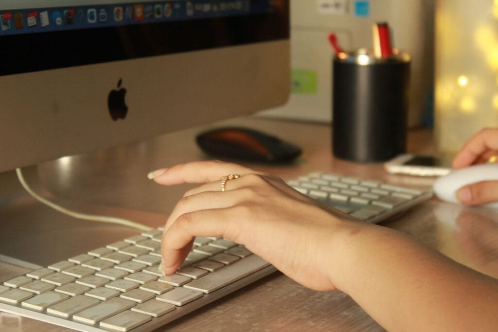 Analista e +vagas remotas com R$ 1.012,50 de VA/VR A close-up of a woman's hand typing on an Apple keyboard in an office setting.