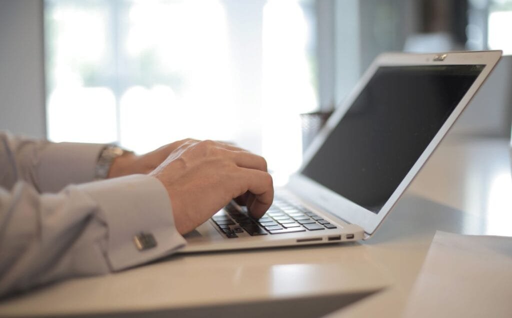 Remotas a Leega com VA de R$ 800,00 Close-up of hands typing on a laptop in a bright, modern office setting.