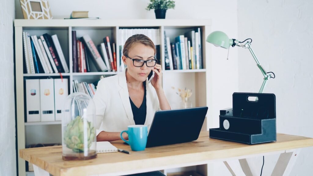 Agro Serra contratando para 100% Home Office Woman on phone at desk with laptop and books
