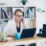 Agro Serra contratando para 100% Home Office Woman on phone at desk with laptop and books