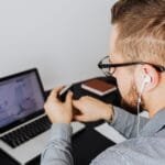 Remotas com VA/VR de R$ 1.200,00 A business professional uses a laptop with charts and graphs while wearing earphones in an office setting.