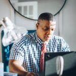 Customer Success e mais remotas com R$ 970 de VA/VR A concentrated adult man working on his laptop in a bright modern office setting.