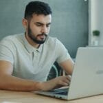 Vagas 100% Remotas na Bernoulli Focused young man typing on a laptop in a contemporary office setting.