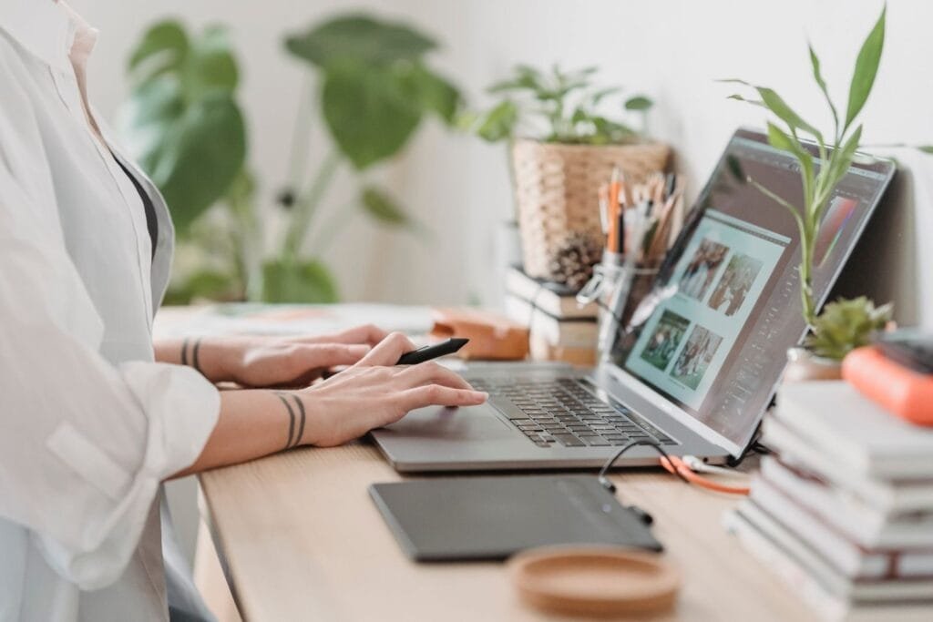 Analista de Segurança e +Remotas com VA/VR de R$ 950,00 Side view of crop anonymous female photographer editing photos on netbook while sitting at table with stylus and graphic tablet