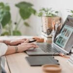Assistente de Atendimento e +Remotas com VA/VR de R$ 950,00 Side view of crop anonymous female photographer editing photos on netbook while sitting at table with stylus and graphic tablet