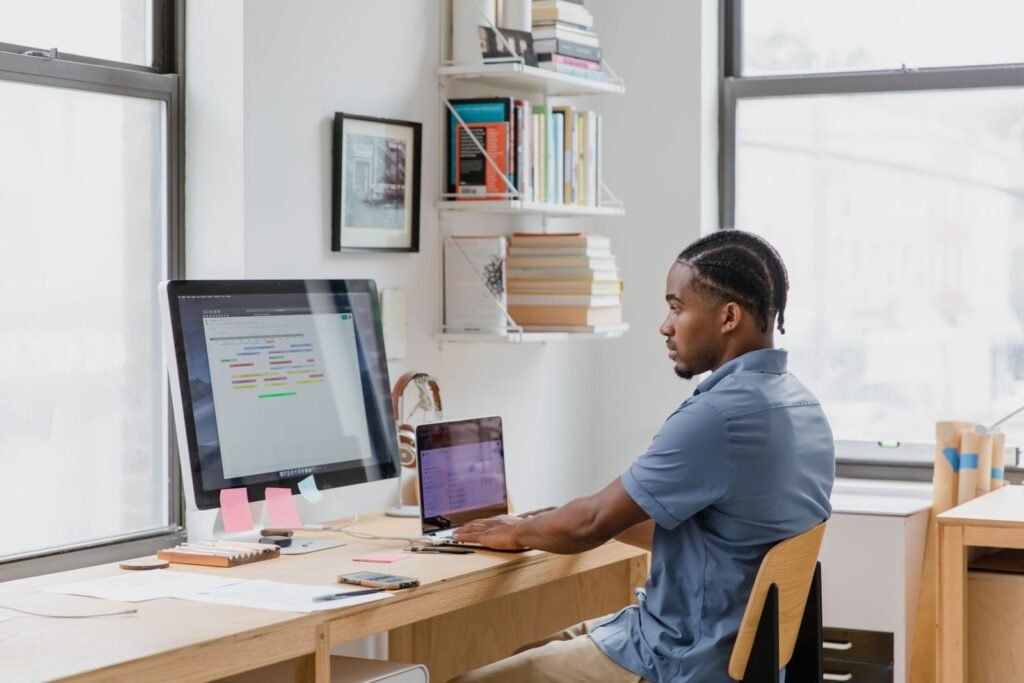 Remotas na SGA com R$ 1.200 de Benefícios Flexíveis Focused man at home office desk working on dual screens. Ideal for remote work themes.