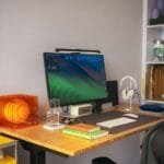 Júnior em Vagas Remotas com R$ 1.012,50 de VA/VR A computer monitor, keyboard, and orange lamp on a wooden desk in a workspace